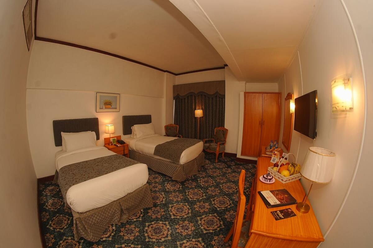 A hotel room with two beds, a desk, a chair, a television, and a patterned carpet.