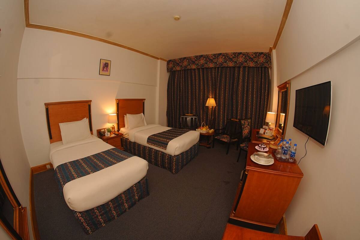 A hotel room with two beds, a desk, a chair, a TV, and a window with curtains.