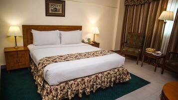 A hotel room with a large bed, two bedside tables with lamps, a chair, and a small table with a lamp.