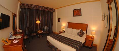 A hotel room with a bed, bedside tables, a desk with a chair, a dining table, and a large mirror.