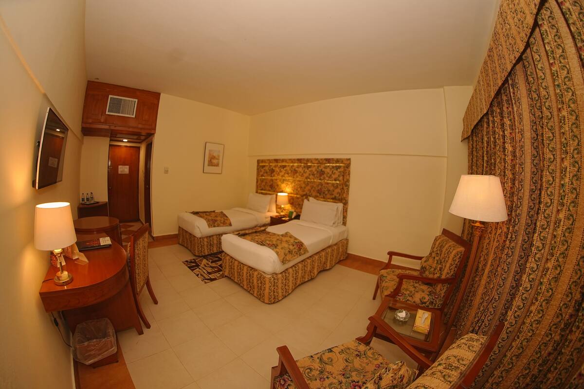 A hotel room with two beds, a desk, a chair, and a television.