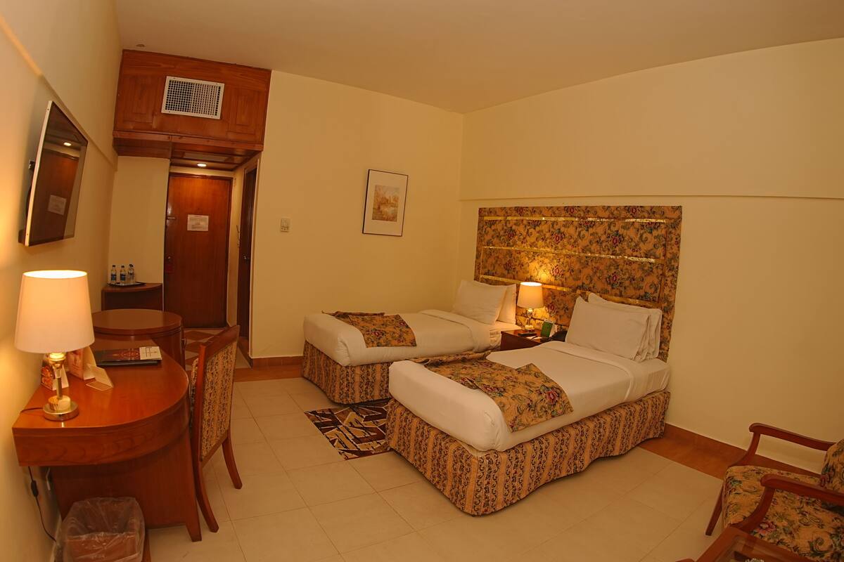 A hotel room with two beds, a desk, a chair, a lamp, and a small rug.