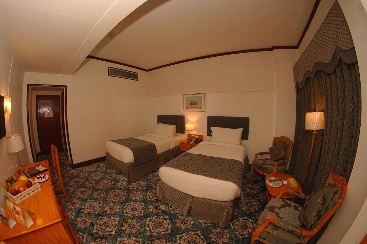 A hotel room with two beds, a desk, a chair, a table, and a patterned carpet.