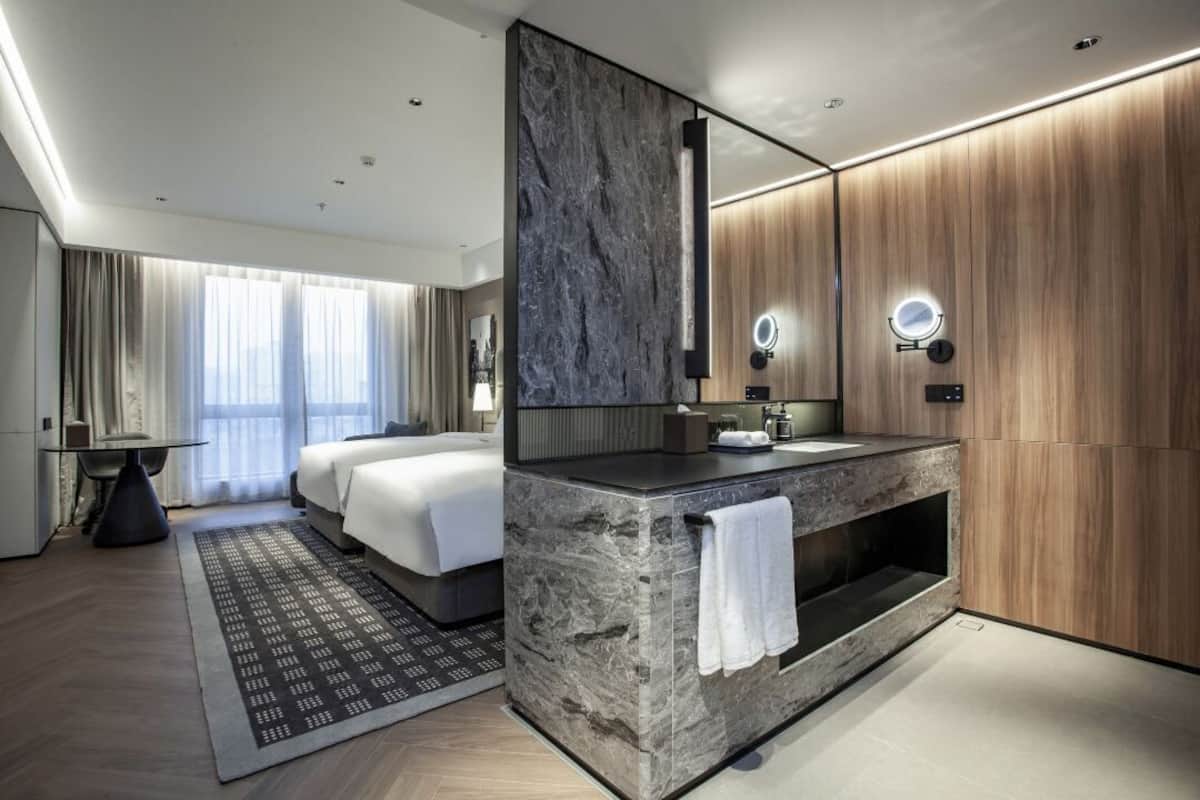 A modern hotel room with a large bed, a vanity with a mirror, and a seating area with a table and chairs.