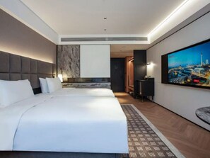 Une chambre d’hôtel moderne dotée d’un grand lit, d’un téléviseur à écran plat, d’une vue sur la ville et d’un petit espace bureau.