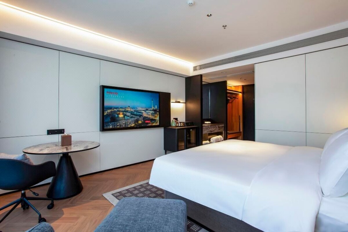 Ein Hotelzimmer mit Bett, Schreibtisch, Stuhl, Fernseher und einem Gemälde.