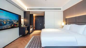 A hotel room with a large bed, a television on the wall, a wardrobe, and a desk with a lamp.