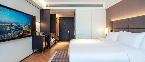 A hotel room with a large bed, a television on the wall, a wardrobe, and a desk with a lamp.