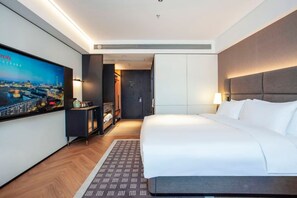 Une chambre d’hôtel avec un grand lit, un téléviseur fixé au mur, une armoire et un bureau avec une lampe.