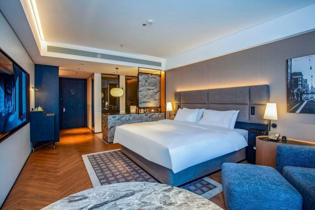 Quarto de hotel moderno com uma cama grande, área de estar, escrivaninha e televisão.