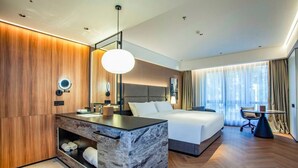 Une chambre d’hôtel moderne avec un meuble-lavabo en marbre, un grand lit, une table ronde et une vue sur la ville par la fenêtre.