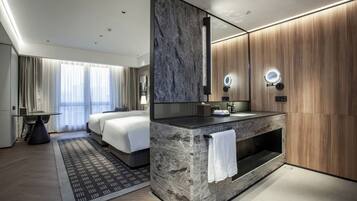 Una habitación de hotel moderna con una cama grande, un tocador con espejo y una zona de estar con una mesa y sillas.