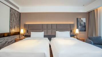 A hotel room with two beds, a headboard, bedside lamps, a sofa, and a painting on the wall.