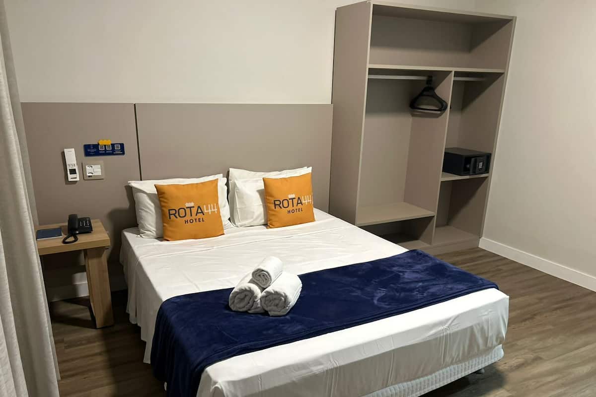 A hotel room with a bed, two pillows with the hotel name, a bedside table with a phone, and a wardrobe.