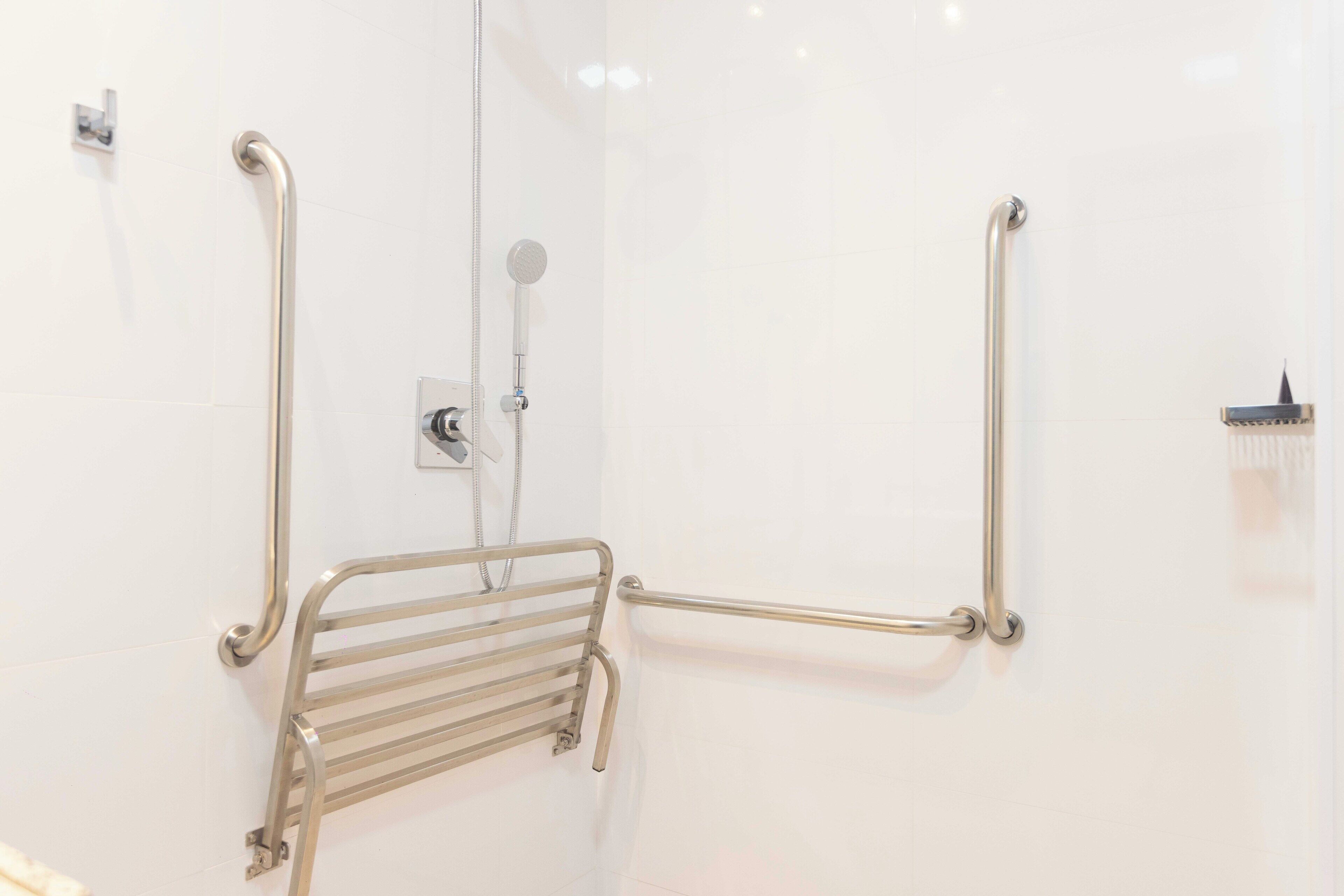 A bathroom with a walk-in shower, grab bars, and a handheld showerhead.
