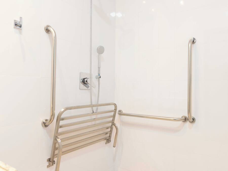 Une salle de bain équipée d’une douche à l’italienne, de barres d’appui et d’un pommeau de douche amovible.