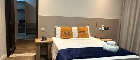 Habitación de hotel con cama, mesita de noche, teléfono y panel de control en la pared.