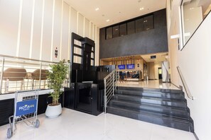 A modern hotel lobby with a reception desk, a potted plant, and a luggage cart.