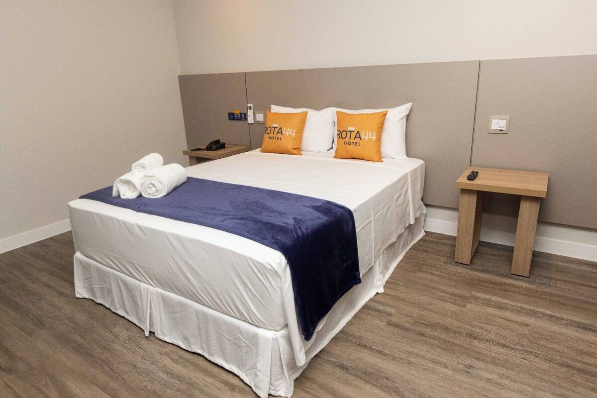 A hotel room with a neatly made bed, a bedside table with a phone, and a small wooden nightstand.