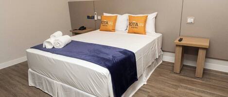 Una habitación de hotel con una cama bien hecha, una mesita de noche con un teléfono y una pequeña mesita de madera.