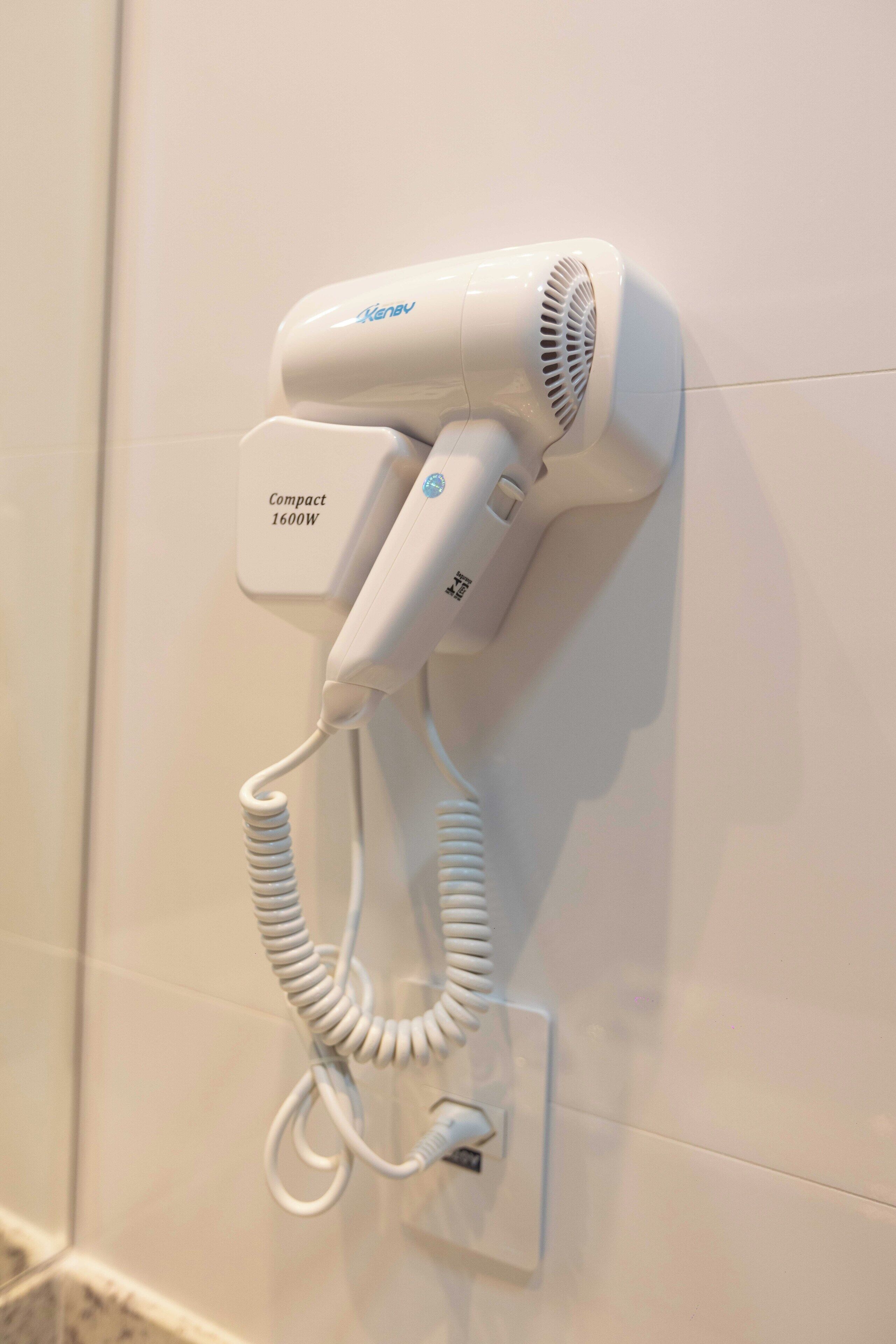 Un secador de pelo montado en la pared, con una etiqueta que indica que es un dispositivo compacto de 1600W.