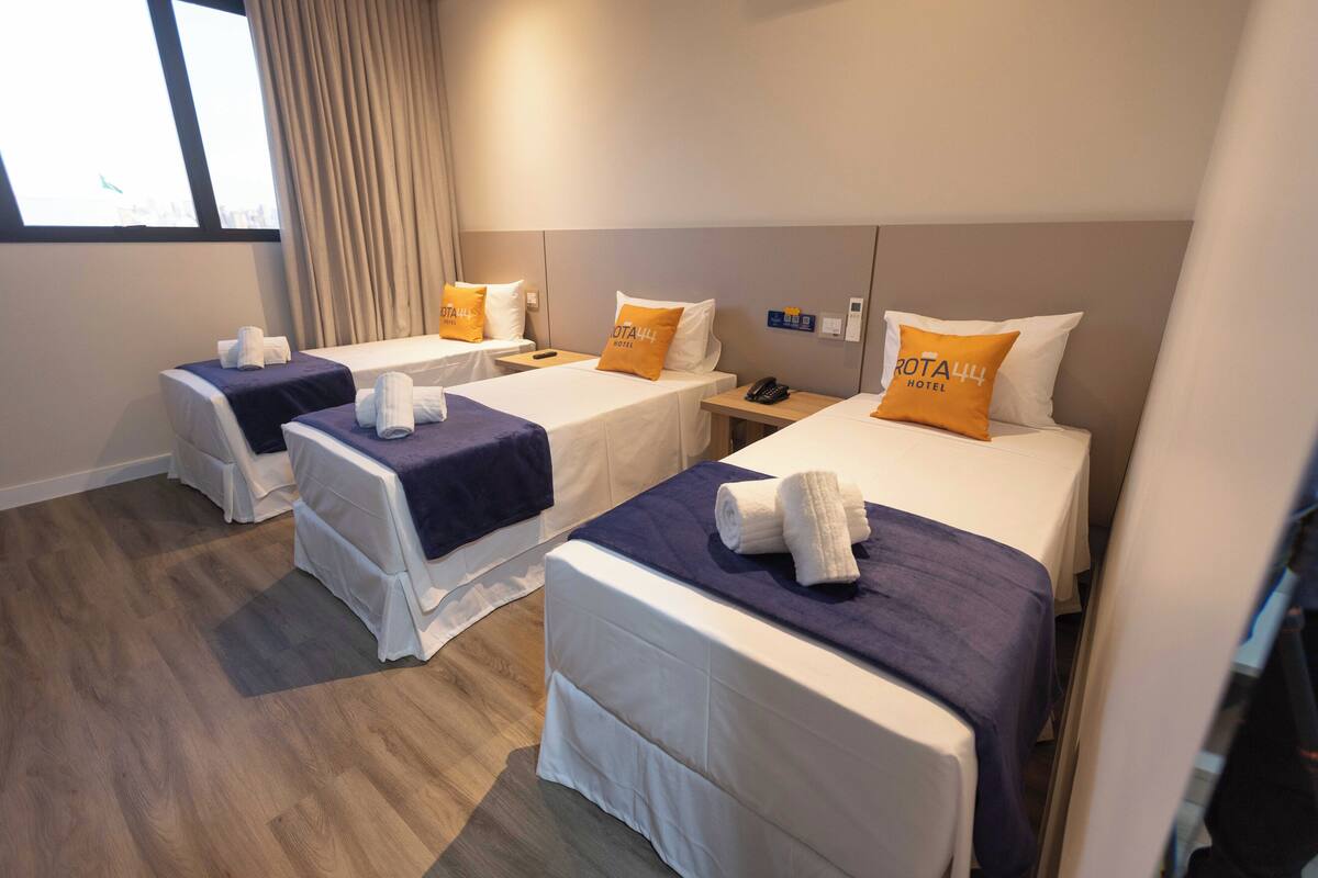 A hotel room with three single beds, each with a pillow and a rolled towel.