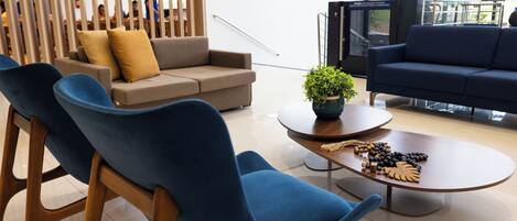 A modern hotel lobby with a seating area featuring blue chairs, a grey sofa, and a wooden partition.
