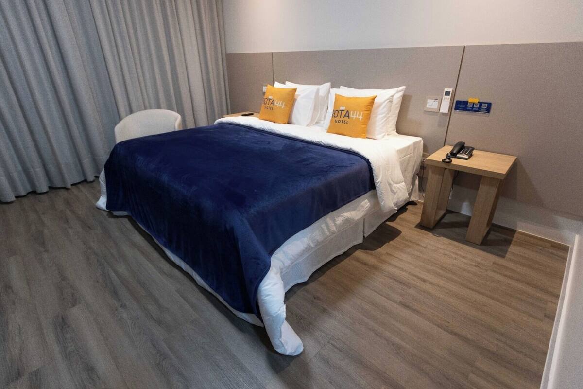 A hotel room with a bed, a bedside table with a phone, and a chair.