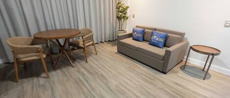 Un salón moderno con un sofá beige, dos almohadas azules, una mesa de comedor de madera con cuatro sillas y una pequeña mesita auxiliar.