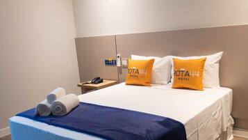A hotel room with a bed, a nightstand, and an air conditioning unit.