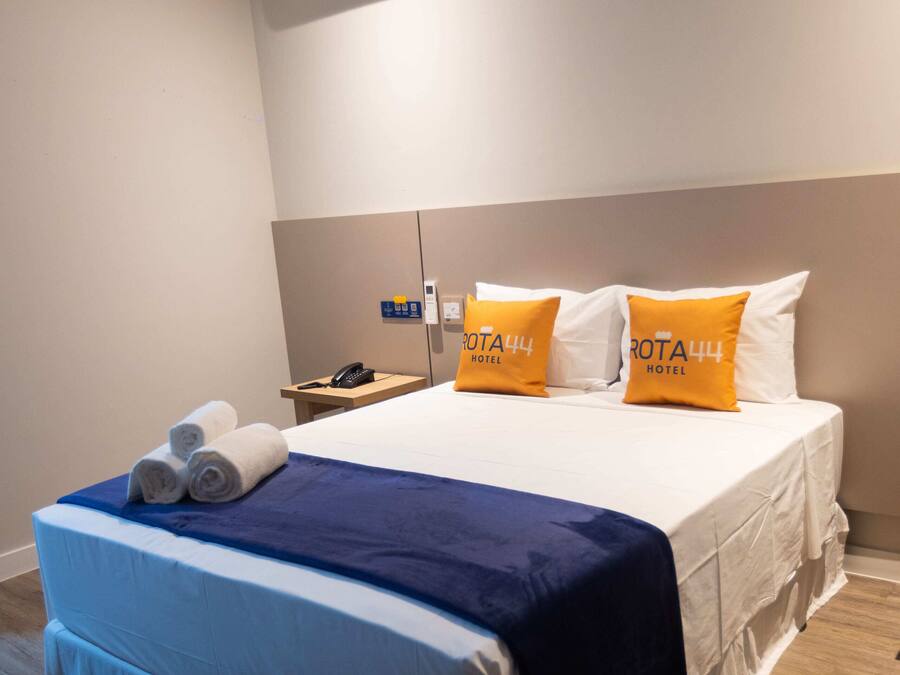 A hotel room with a bed, a nightstand, and an air conditioning unit.