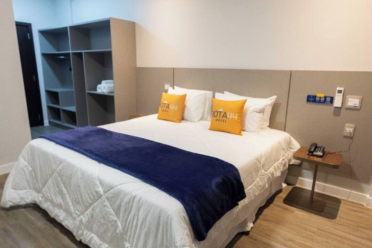 A modern hotel room with a large bed, a bedside table with a phone, and a storage unit.