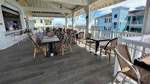 Un espacio de comedor al aire libre techado con mobiliario de mimbre y vistas a edificios costeros.