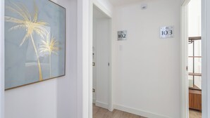 A hallway with a framed artwork of palm trees, a door with a number sign, and a staircase visible in the background. - Rhome Vatican Rooms (Rome)
