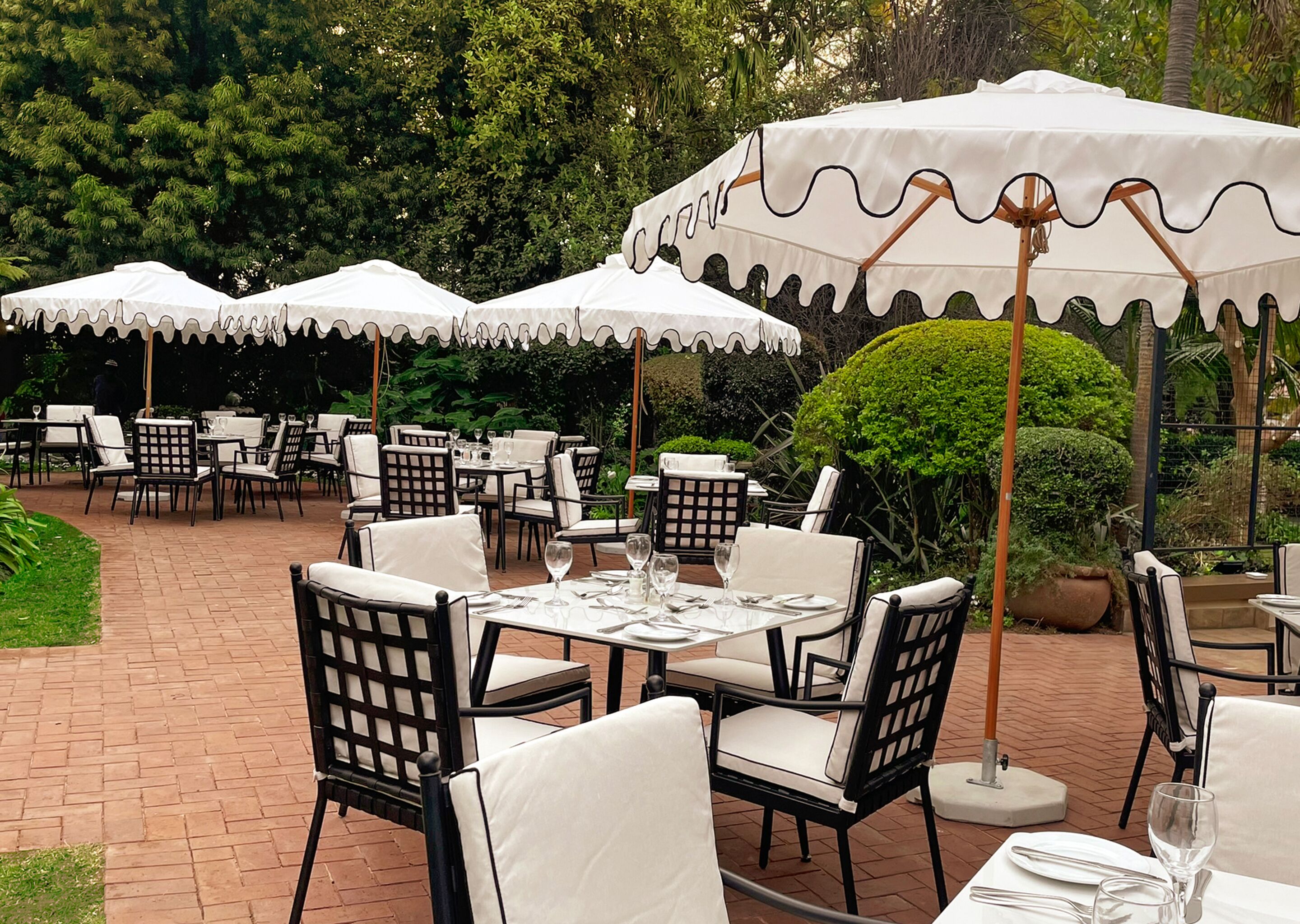 Un área de comedor al aire libre con mesas y sillas bajo sombrillas blancas, rodeada de follaje.