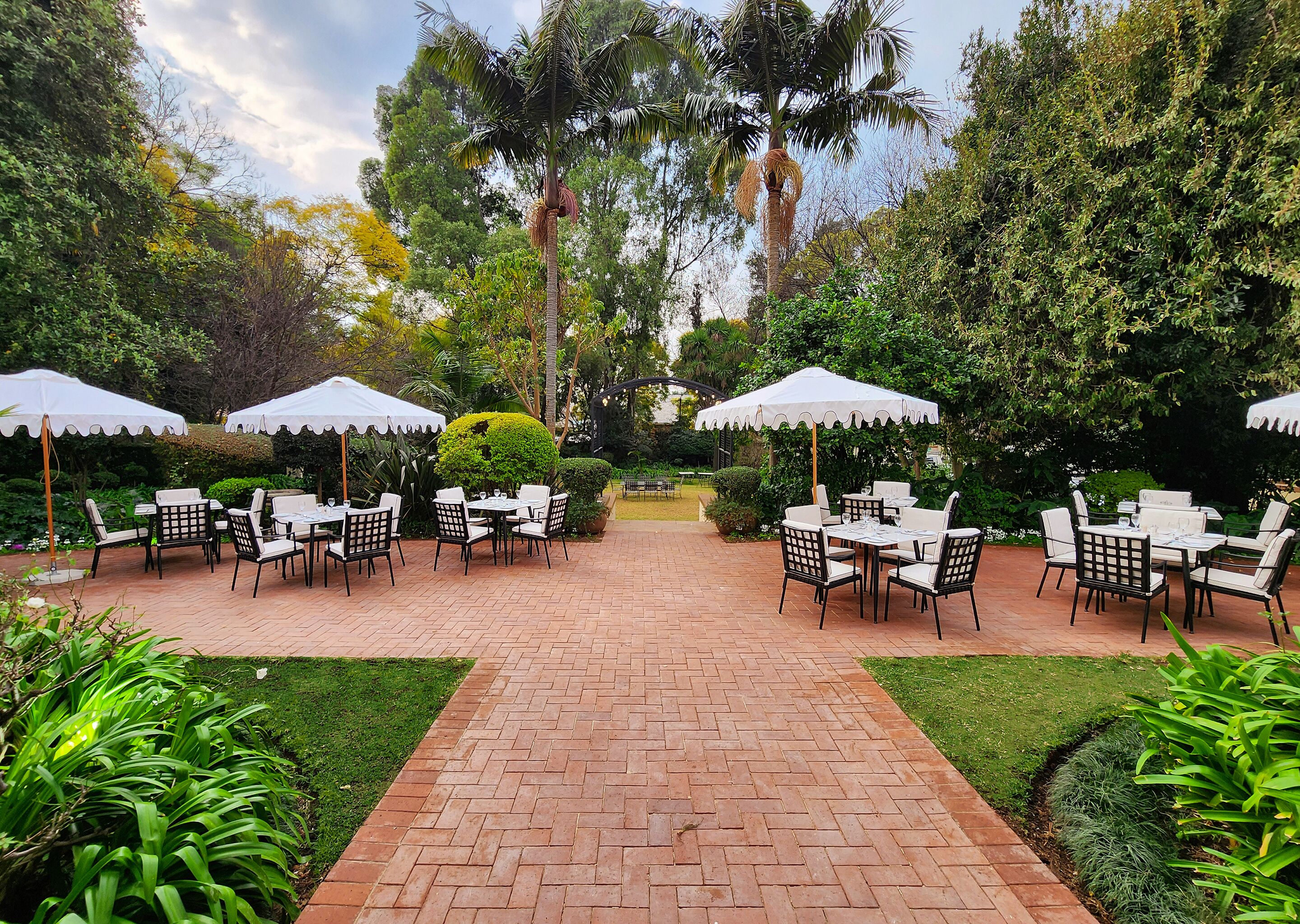 An outdoor patio with brick flooring, white tables and chairs, and white umbrellas.