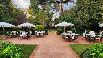 An outdoor patio with brick flooring, white tables and chairs, and white umbrellas.