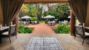 Un patio interior con mesas y sillas, una lámpara de araña y vistas al jardín exterior.