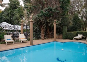 A swimming pool with lounge chairs and umbrellas, surrounded by dense foliage and a decorative fence. - 10 2nd Avenue Boutique Hotel by Dream Resorts (Johannesburg)