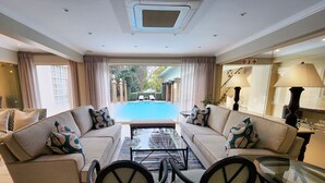 Amplia sala de estar con una mesa de centro de vidrio, dos sofás con cojines estampados y vista a una piscina.