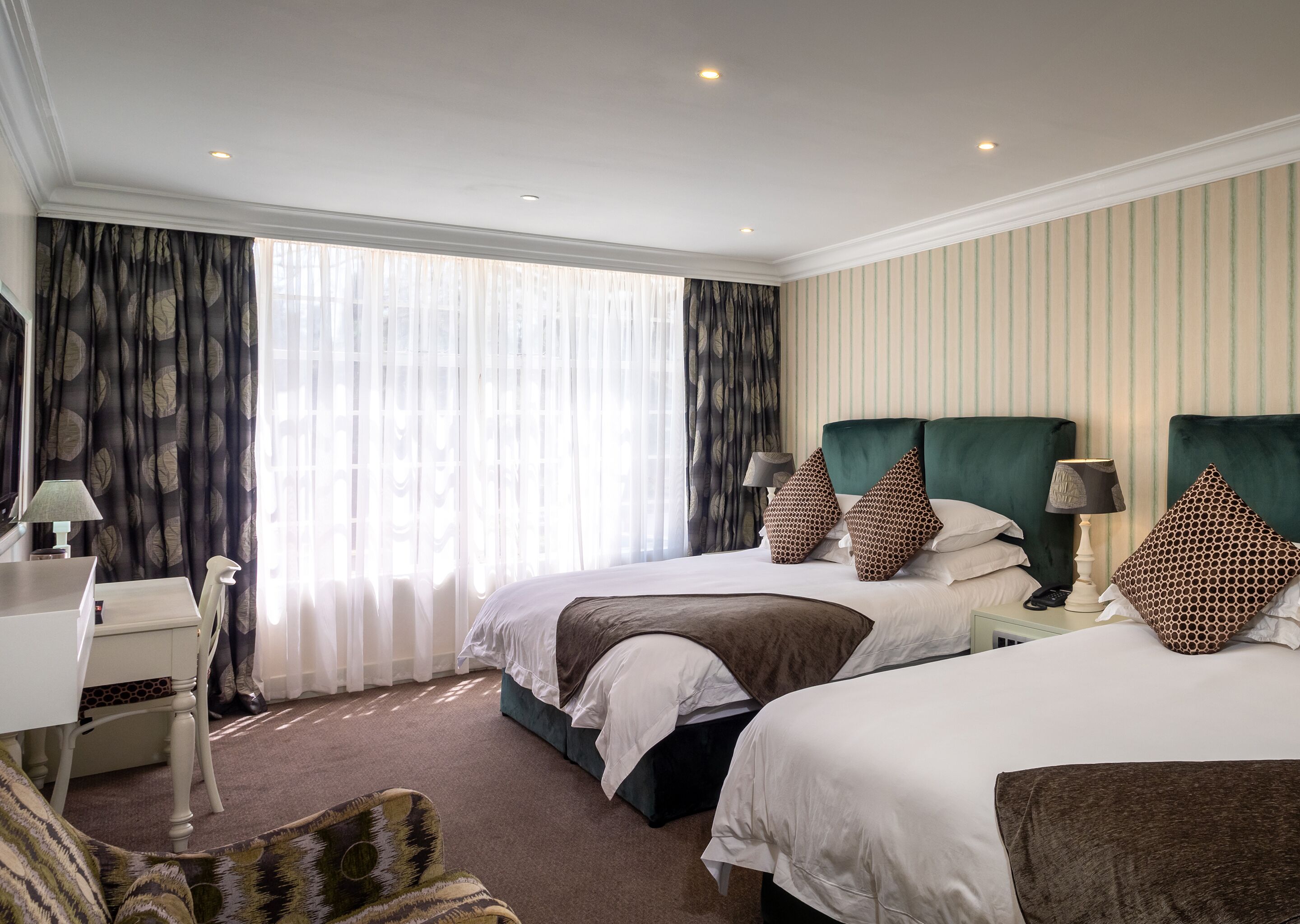 A hotel room with two beds, a desk, a chair, and a window with curtains.