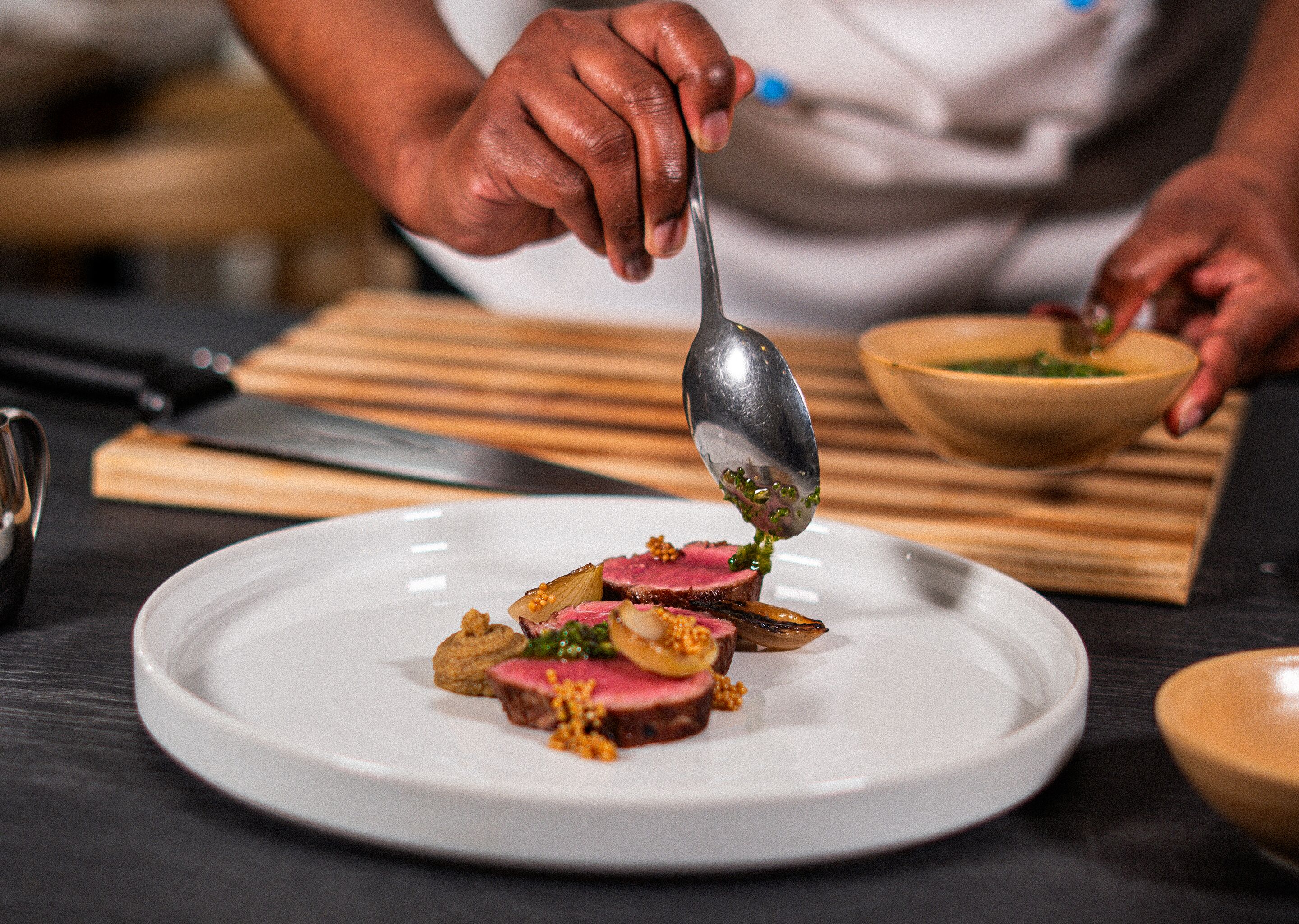 A chef plating a dish on a white plate.