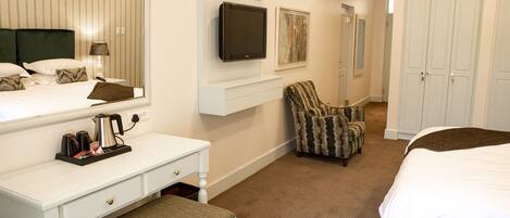 Quarto de hotel com cama, escrivaninha com cadeira, televisão e guarda-roupa.