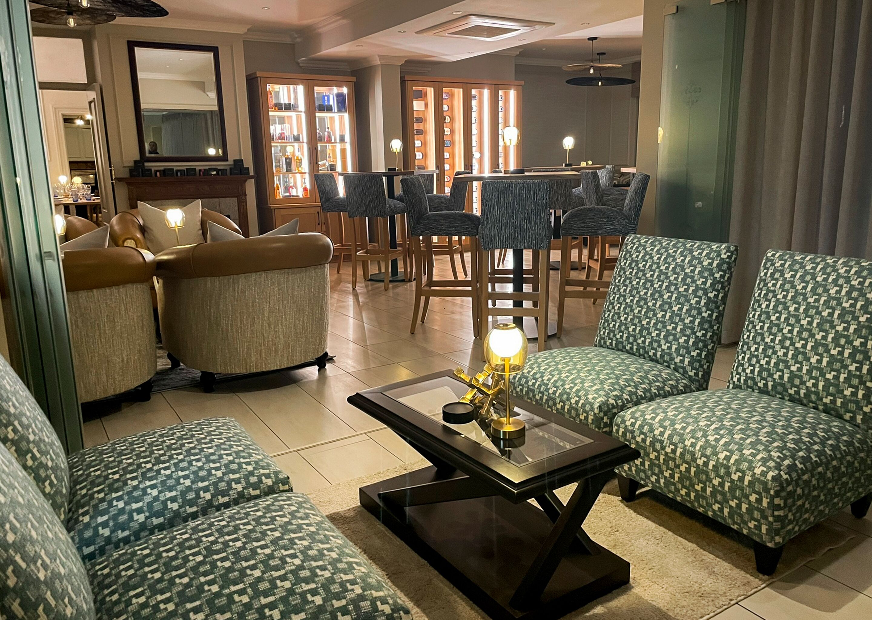 A spacious living room with patterned sofas and armchairs, a coffee table with decorative items, and a dining area in the background.