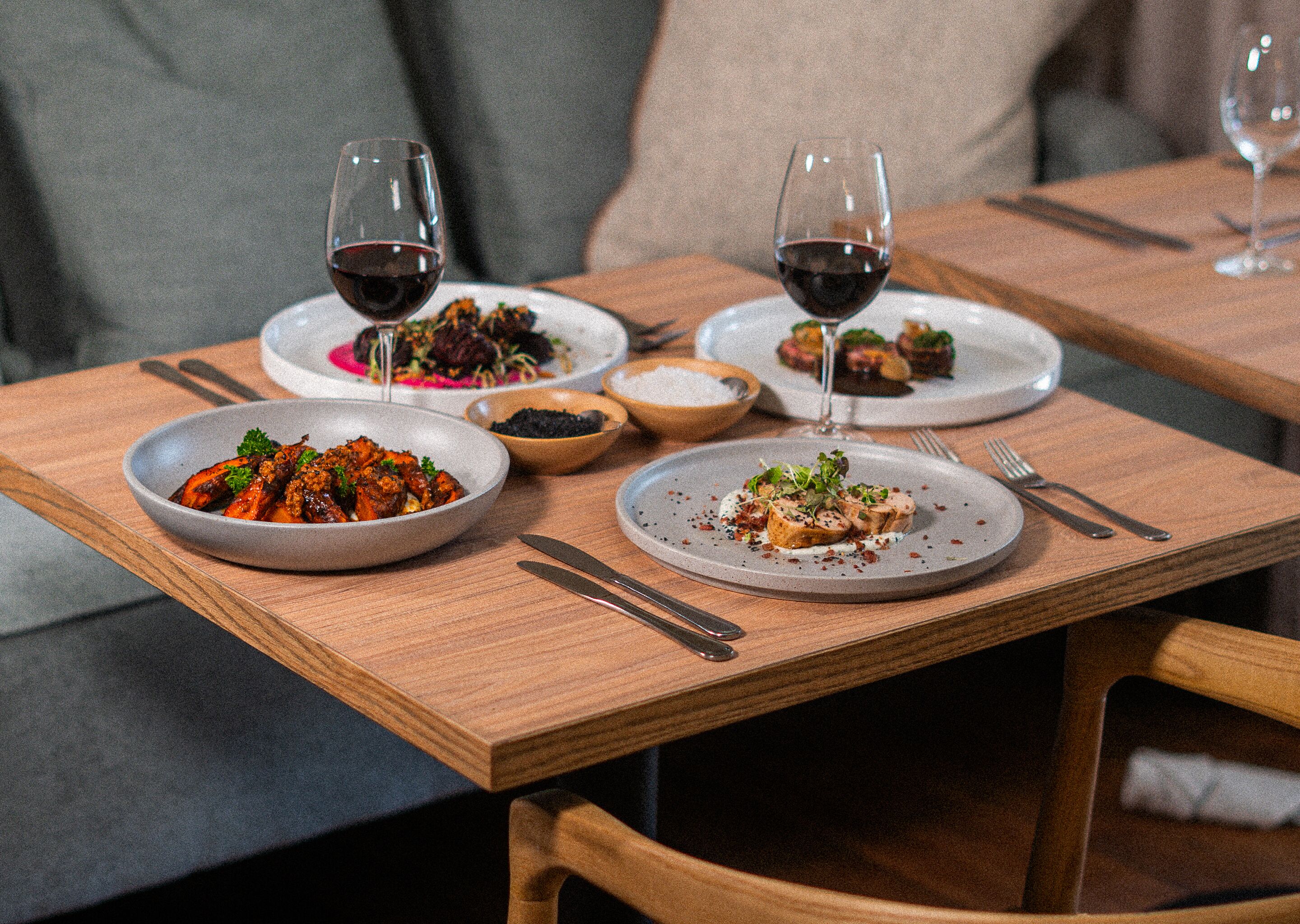 A dining table with plates of food, glasses of red wine, and cutlery.