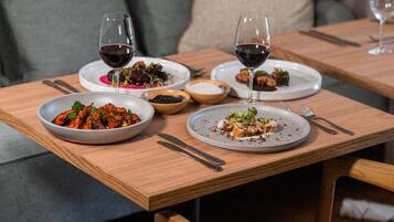 A dining table with plates of food, glasses of red wine, and cutlery.