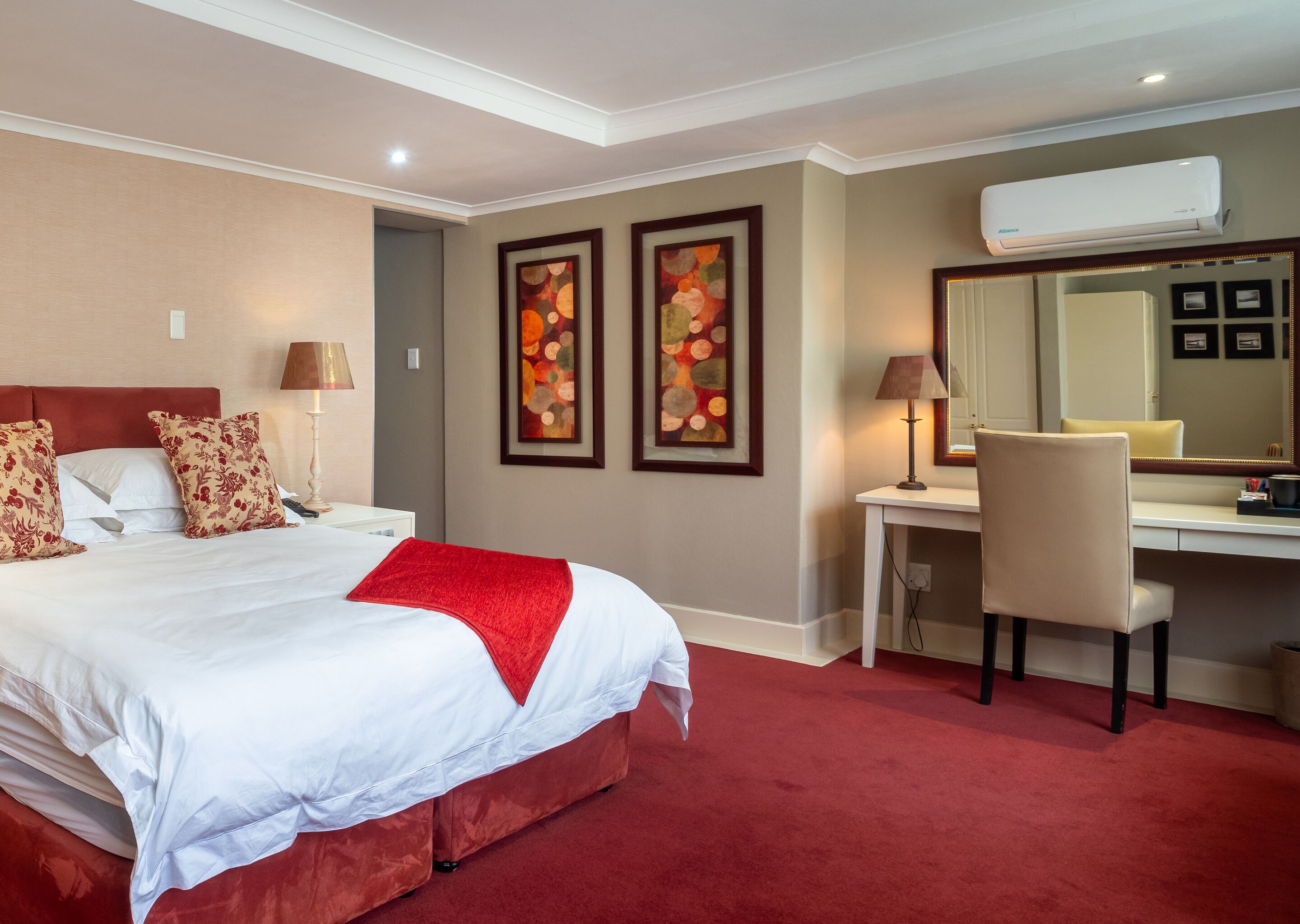 A hotel room with a large bed, a desk, a chair, and two framed artworks on the wall.