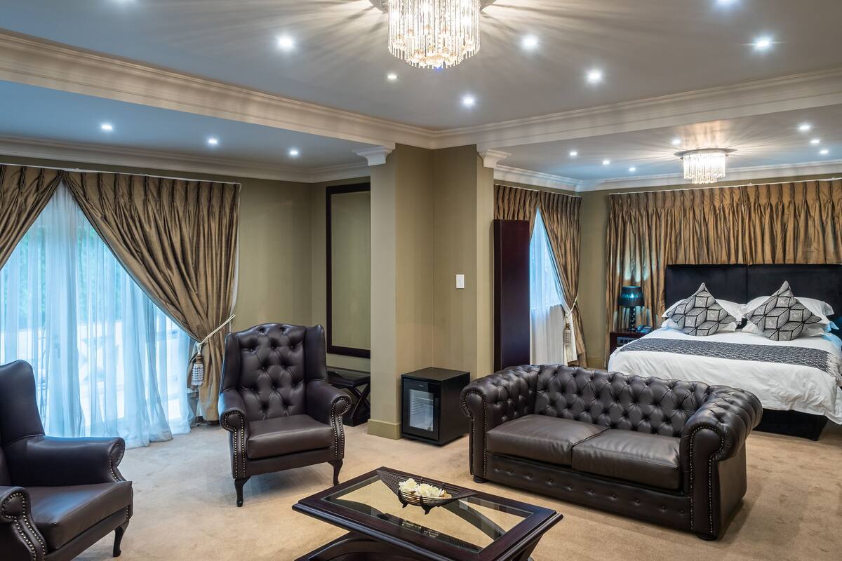 A luxurious bedroom with a large bed, a chaise lounge, a leather armchair, and a glass coffee table.