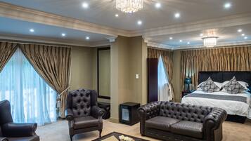 A luxurious bedroom with a large bed, a chaise lounge, a leather armchair, and a glass coffee table.