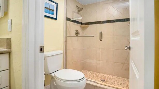 Un bagno con un WC, una doccia con porta in vetro e pavimento piastrellato.